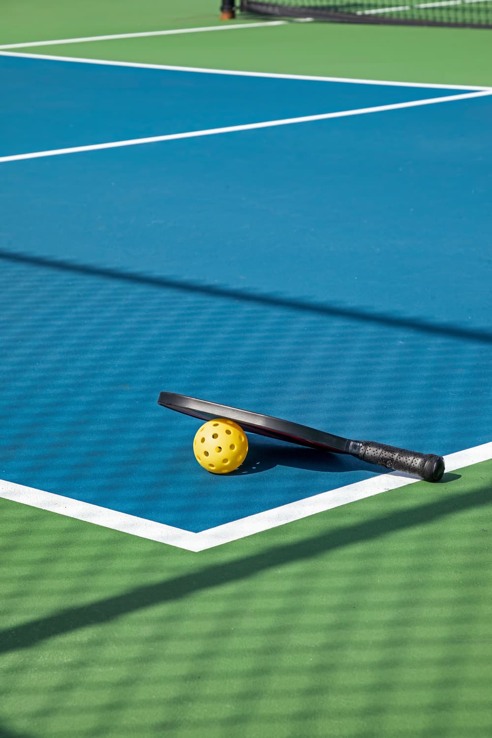 Picture of a paddle and pickleball on a blue and green pickleball court.